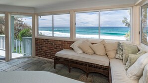 A sunroom with a view of the ocean, a brick wall, and a cushioned bench.