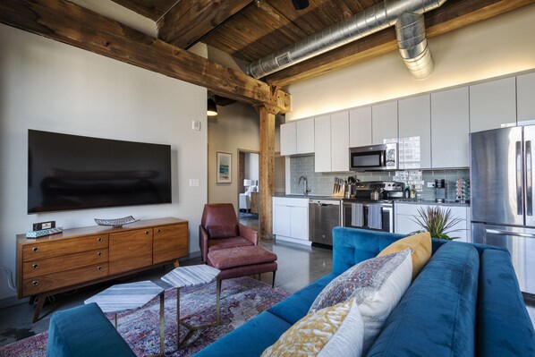 A modern kitchen with stainless steel appliances, a wooden ceiling, and a blue sofa in the living area.