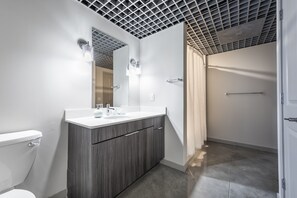 A modern bathroom with a white toilet, a wooden vanity with a white countertop, a mirror, and a shower area with a glass door.