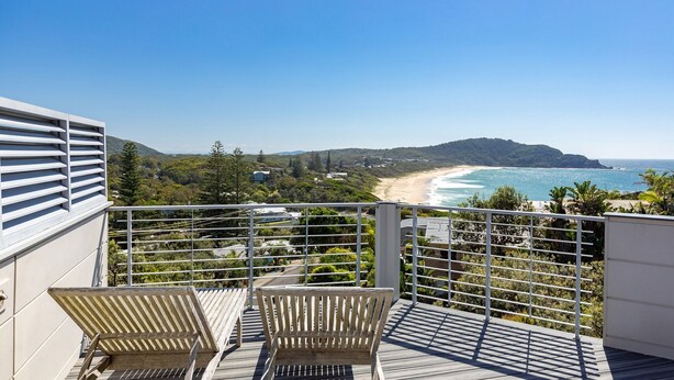 Ein Balkon mit zwei Holzstühlen, mit Blick auf Strand und Meer.