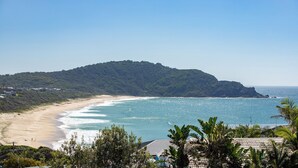 Ein Strand mit einem Berg im Hintergrund, klarem Himmel und einigen Gebäuden nahe der Küste.