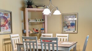 Een eetkamer met een houten tafel en stoelen, een kroonluchter, lijstwerken en een plank met decoratieve objecten.