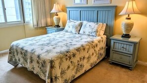 Een slaapkamer met een bed, twee nachtkastjes, een raam met gordijnen en twee aan de muur bevestigde foto's.