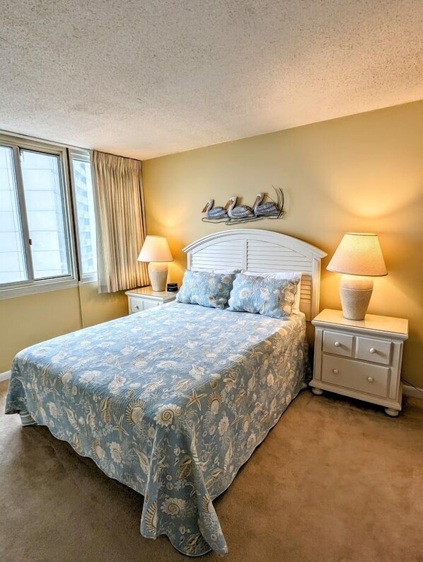 A bedroom with a large bed, two bedside tables with lamps, a window with curtains, and a wall decoration of birds.