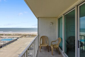 Un balcon avec deux chaises, une piscine et une vue sur la plage et l’océan.