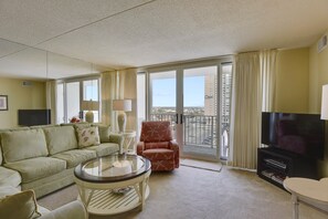Een hotelkamer met een bank, fauteuil, televisie en een balkon met uitzicht over de stad.