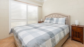 A bedroom with a bed, a nightstand, a lamp, and a window with blinds.