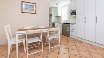 A dining area with a white table and chairs, a kitchen with white cabinets and a microwave, and a tiled floor.