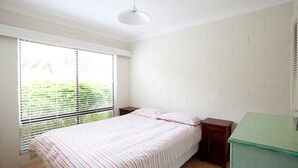 A bedroom with a bed, a nightstand, a window with blinds, and a green cabinet. - Blueys Beach Villa Manyana 24 (Blueys Beach)