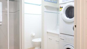 Une petite salle de bain propre, dotée d’une douche à parois de verre, de toilettes et d’un lave-linge et d’un sèche-linge superposés.