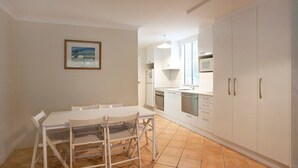 A compact kitchen with white cabinets, a dining table with chairs, and a tiled floor. - Blueys Beach Villa Manyana 24 (Blueys Beach)