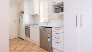 Une cuisine compacte avec des meubles blancs, un lave-vaisselle, un four et un four à micro-ondes.