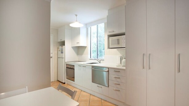 A modern kitchen with white cabinets, a built-in oven, a microwave, and a window with blinds. - Blueys Beach Villa Manyana 24 (Blueys Beach)