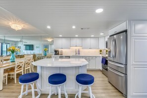 Cozinha moderna com armários brancos, uma ilha central com banquetas e eletrodomésticos de aço inoxidável.