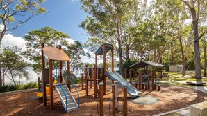 Un parque infantil con tobogán y estructuras para escalar, rodeado de árboles y una zona de picnic.