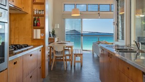 A modern kitchen with wooden cabinets, a gas stove, and a view of the sea through large windows. - Sea Shack - at Seal Rocks (Seal Rocks)