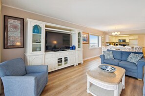 Ein Wohnzimmer mit Fernseher, weißen Schränken, einem blauen Sofa und einem Essbereich mit Tisch und Stühlen.