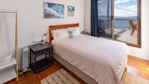 A bedroom with a large bed, a bedside table with a lamp, a chair, and a view of the sea through a window.