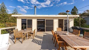 A covered patio with a dining table and chairs, a barbecue grill, and a view of a house with sliding glass doors.