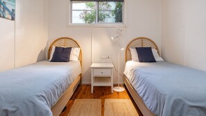 A room with two single beds, a small bedside table, a power outlet, and a window with a view of trees.