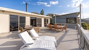 A covered outdoor patio with a table and chairs, a grill, and lounge chairs.