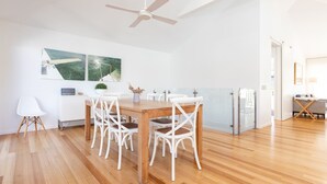 A modern kitchen with a wooden dining table, white chairs, and a ceiling fan. - Banksia - Pacific Palms Holidays (Blueys Beach)
