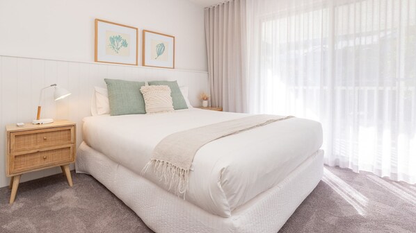 Ein ordentlich eingerichtetes Schlafzimmer mit einem großen Bett, einem Nachttisch mit Lampe und zwei gerahmten Pflanzenbildern an der Wand.