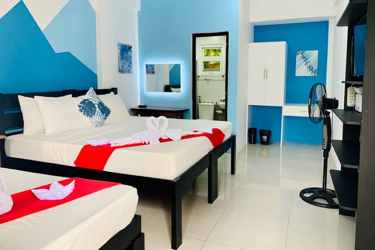 A hotel room with two beds, a desk, a mirror, and a fan.