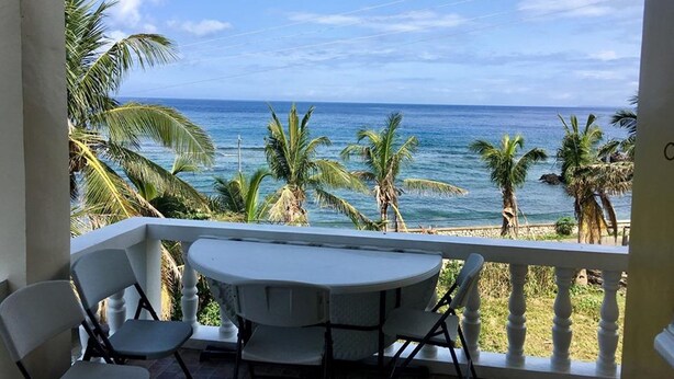 Un balcón con mesa y sillas que da a una playa con palmeras y el océano.