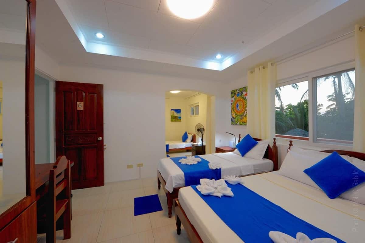 A hotel room with two beds, a wooden desk, a chair, and a large window.