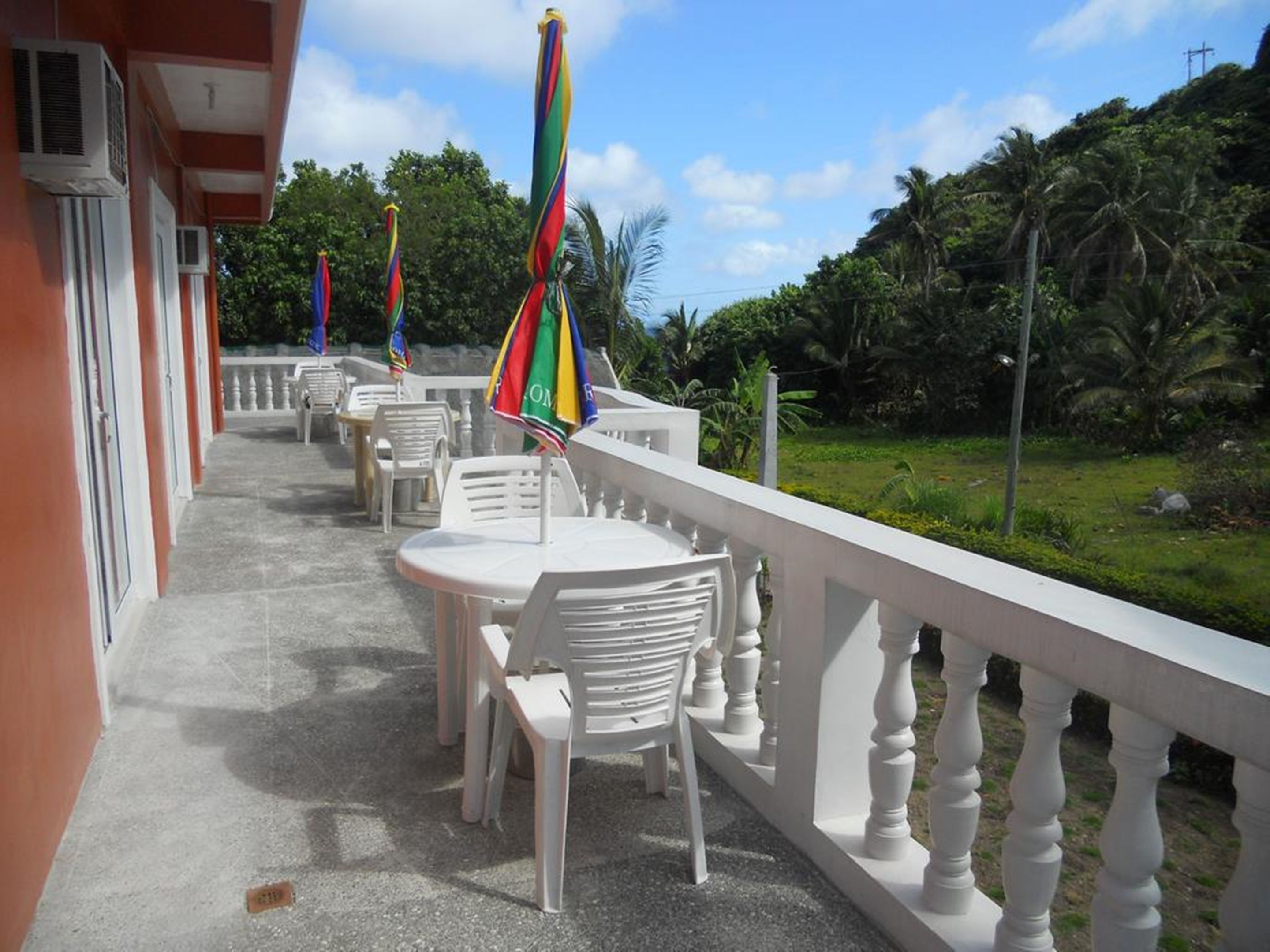A balcony with white chairs and tables, a white railing, and colorful umbrellas.