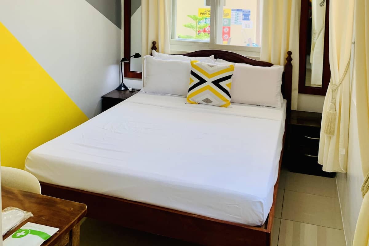A hotel room with a bed, a nightstand, a bedside table, a window with curtains, and a view of the outside.