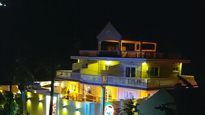 Un edificio de varios pisos con piscina al frente, iluminado con luces artificiales.