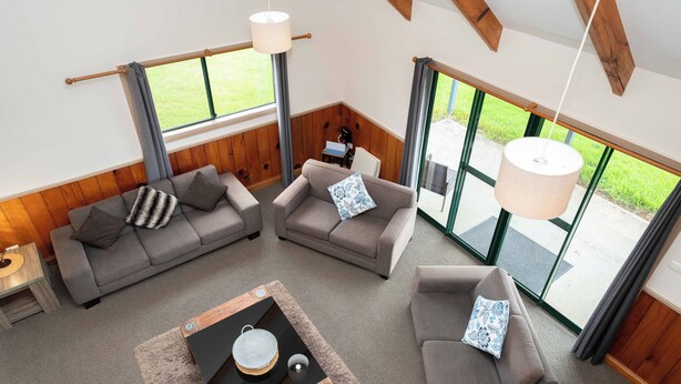 A spacious living area with two sofas, a coffee table, and large windows offering a view of the outdoors. - Ferny Lane House (Norfolk Island)