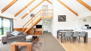 A spacious living area with a high ceiling, wooden beams, a sofa, a coffee table, and a dining area with chairs and a table. - Ferny Lane House (Norfolk Island)