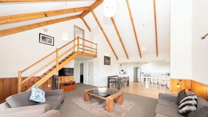 A spacious living area with a wooden staircase, a dining table, and a kitchen in the background. - Ferny Lane House (Norfolk Island)