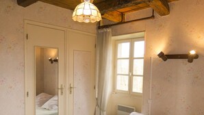 Et soveværelse med seng, garderobeskab, spejl, et vindue med gardiner og en vægmonteret lampe.