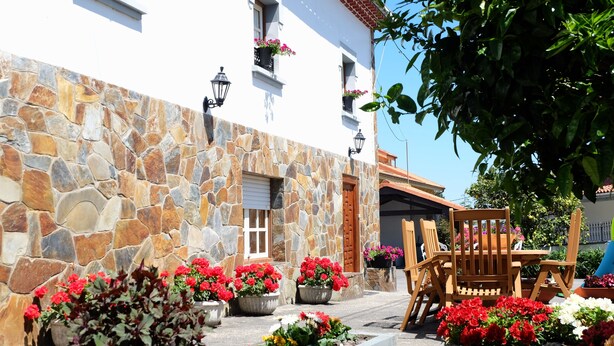 Un edificio de piedra con fachada blanca, muebles de madera y macetas con flores.