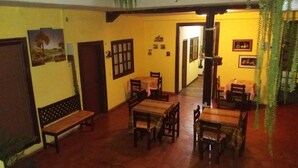 Una zona de menjador amb taules i bancs de fusta, parets grogues i un passadís que condueix a una altra estança.