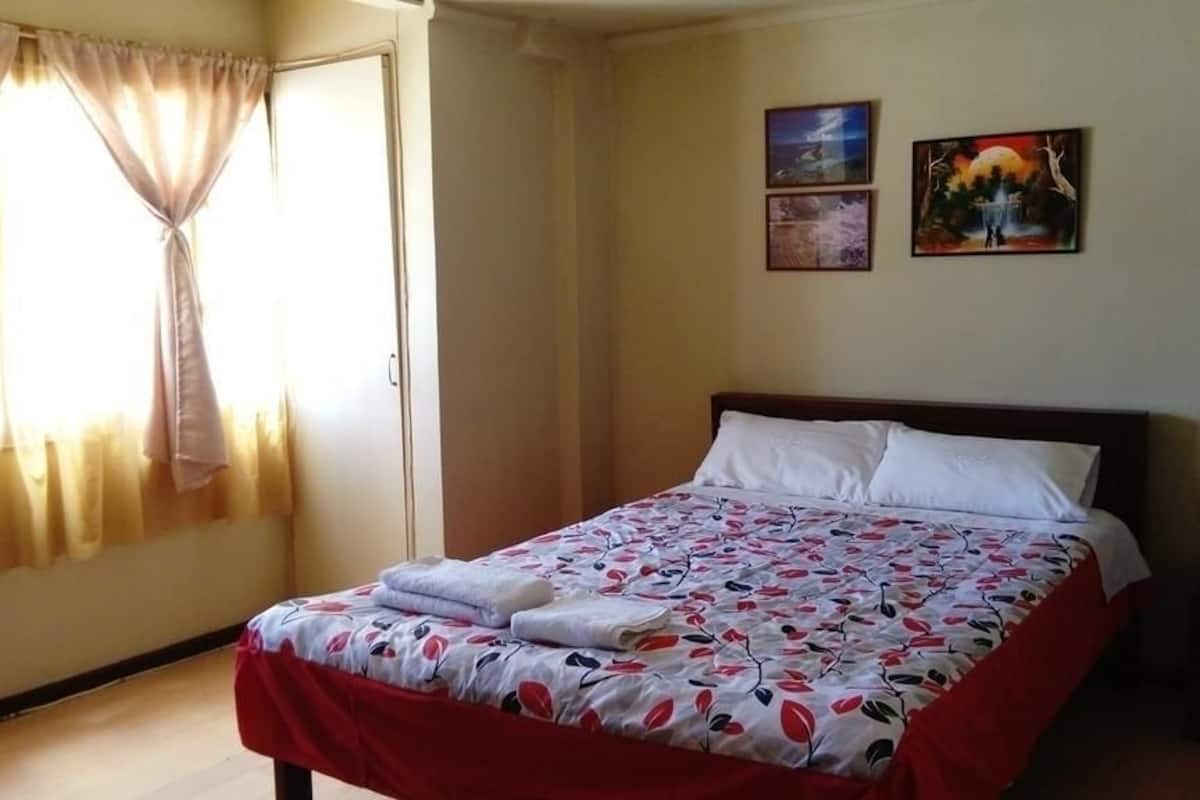 A hotel room with a bed, a nightstand, a lamp, and two paintings on the wall.