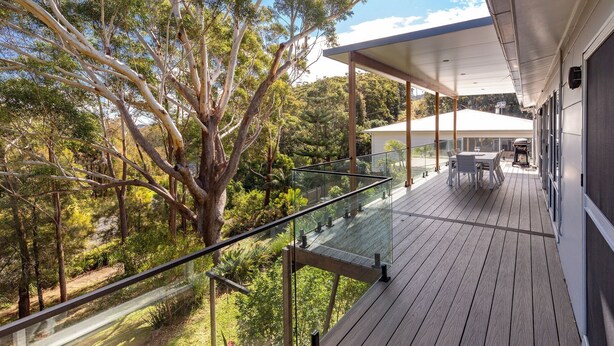 Varanda com guarda-corpo de vidro com vista para uma área arborizada.