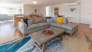 Uma sala de estar moderna com um sofá modular, uma mesa de centro e um espaço de jantar com mesa e cadeiras de madeira.