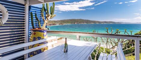 A wooden deck with a table, a potted cactus, and a bottle of champagne.