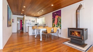 A modern kitchen with white cabinets, a dining area with wooden chairs, and a wood-burning stove. - The Shack - at Seal Rocks (Seal Rocks)