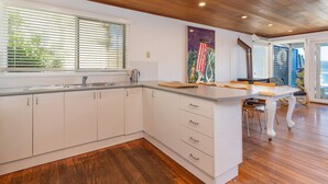 A modern kitchen with white cabinetry, a wooden countertop, and a view of the ocean through large windows. - The Shack - at Seal Rocks (Seal Rocks)