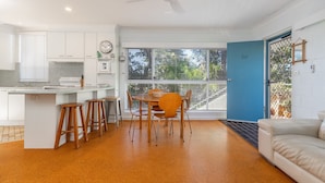 Una cucina moderna con mobili bianchi, un'area pranzo con sedie in legno e una porta blu che dà su un balcone.