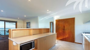 A modern kitchen with wooden cabinets, a built-in microwave, and a view of the ocean.