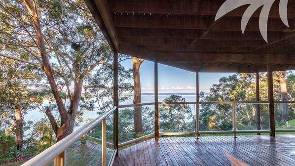 A wooden deck with glass railings overlooking a body of water and trees.
