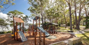 A playground with slides and climbing structures, surrounded by trees and a picnic area.