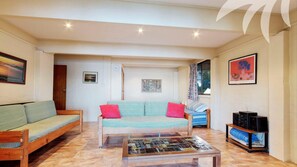 A cozy living room with a wooden sofa, a striped sofa, a coffee table with a mosaic top, and a television on a stand.